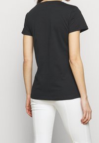 Camiseta negra de manga corta con cuello redondo y forma ajustada, hecha de tela de algodón, vista desde la parte de atrás.