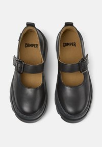 Zapatos de cuero negro con punta redondeada, una correa con hebilla y suela de goma negra gruesa. El interior cuenta con un acolchado color marfil con el logotipo.