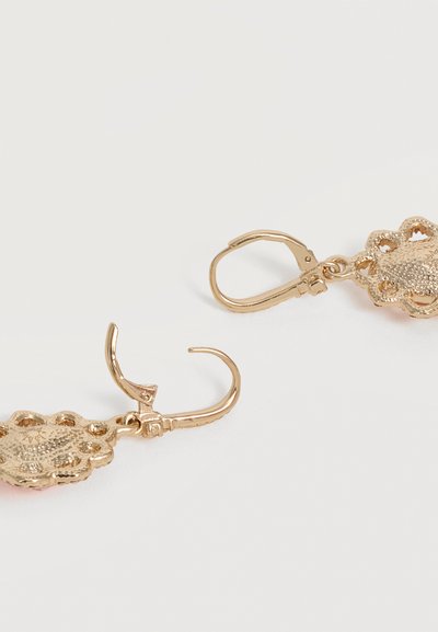 Σκουλαρίκια από μέταλλο σε χρυσαφί απόχρωση με περίπλοκα λουλουδάτα και καρδιόσχημα μοτίβα με ανοίγματα και κλείσιμο με μοχλό σε λευκό φόντο.