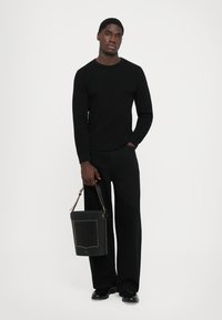 Black ribbed long-sleeve sweater, black wide-leg trousers, black bag with pleated detail and gold accents, black shoes, neutral background.
