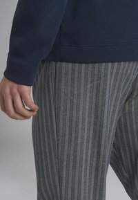 Felpa blu navy con maniche lunghe abbinata a pantaloni a spina di pesce bianco e nero. Il tessuto appare liscio con una vestibilità comoda.