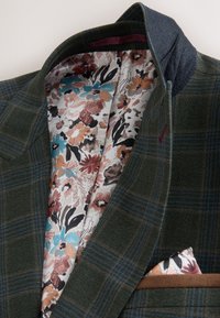 Green plaid jacket with floral patterned lining in shades of blue, brown, and black, and a matching floral pocket square visible.