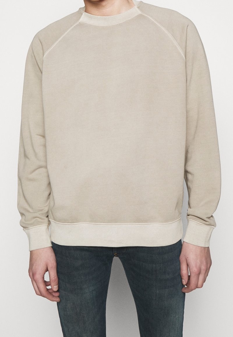 Beżowy sweter z okrągłym dekoltem, rękawami raglanowymi i ściągaczem na dole. Miękka tekstura, minimalistyczny design bez wzorów czy akcentów.
