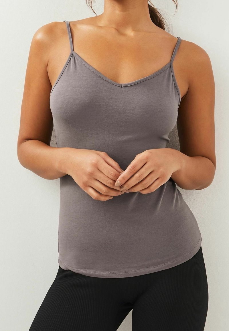 Débardeur gris ajusté avec de fines bretelles et un décolleté en V, en tissu lisse, associé à un legging noir à côtes.