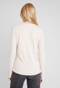Maglione a maniche lunghe di un beige chiaro con una texture morbida, vestibilità rilassata e scollatura tonda. Abbinato a jeans dritti grigi scuri.