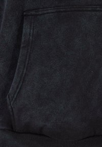 Juodas džemperis iš minkštos medžiagos, su priekinėje dalyje esančia kišenė ir banguotu kraštu. Minkštas, šiek tiek šukuotas vidus, užtikrinantis patogumą.