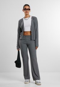 Szürke bordázott kardigán egy fehér cropped top fölött, szürke trapéz nadrággal és fehér edzőcipővel párosítva. Kiegészítők között szerepel egy fekete táska és napszemüveg.