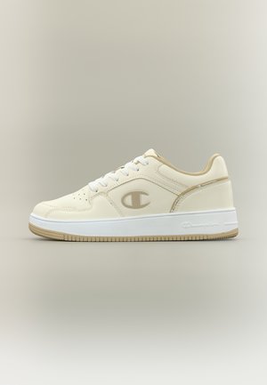 Low-top beige sneaker with white laces, beige interior lining, Champion logo on side and sole, and textured tan outsole.