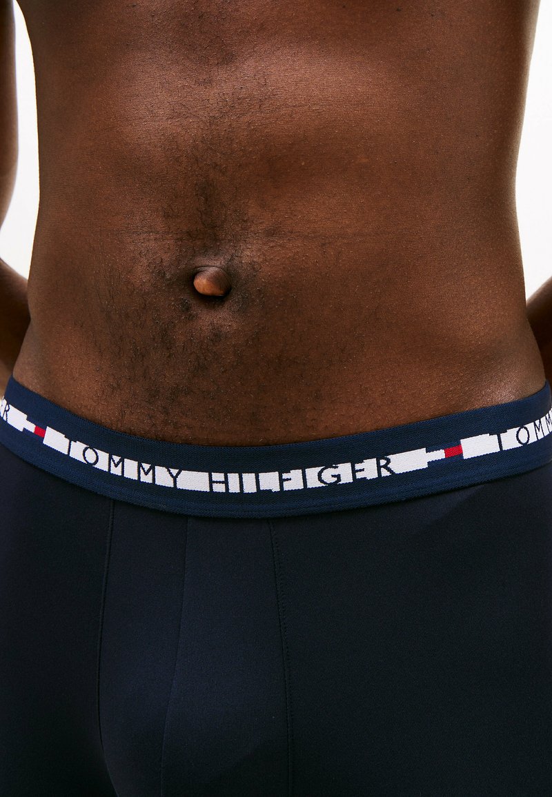 Boxer-joes bleu marine avec une ceinture de marque contrastante blanche et rouge, dotés d'une texture lisse et d'un design ajusté.