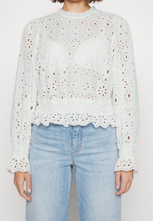 Witte blouse met lange mouwen van bloemen-uitsparingskant, met een geplooide taille en manchetten, gecombineerd met lichtblauwe jeans met hoge taille.