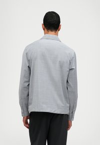 Chemise grise à manches longues avec une coupe décontractée, en tissu texturé et avec des poignets boutonnés ; elle présente un col classique et un ourlet droit.