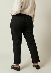 Jeans neri a vita alta con gamba affusolata e tasche posteriori. Il tessuto appare resistente con leggera texture. Abbinati a mocassini neri.