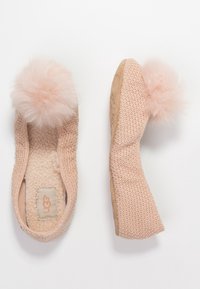 Měkké růžové pletené pantofle s načechranými bambulemi na prstech, s ovčí vlnou uvnitř a protiskluzovou podrážkou, vystavené z horního a bočního pohledu.