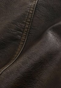 Mørkebrun læderstof med synlig kornstruktur og detaljeret syning, der løber diagonalt over overfladen.