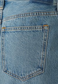 Hele sinine denim kangas, millel on üks tagatasku, nähtavate oranžide õmblustega. Tekstuur paistab olevat veidi kulunud ja pleekinud.