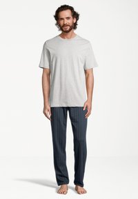 T-shirt en coton gris associé à un pantalon de détente bleu à rayures. Le pantalon présente des rayures blanches verticales et une coupe décontractée. Position pieds nus.