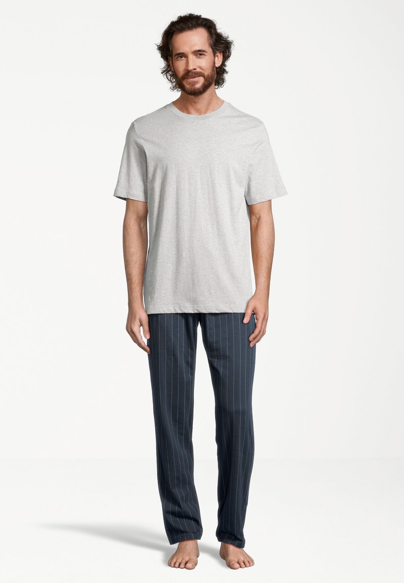 Grijze katoenen t-shirt gecombineerd met blauw gestreepte loungebroeken. De broeken hebben verticale witte strepen en een relaxed fit. Blote voeten.