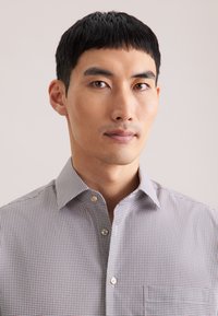 Camicia grigia a quadri con collo button-down, dotata di una tasca sul lato sinistro e di un motivo testurizzato sottile, realizzata in tessuto leggero.