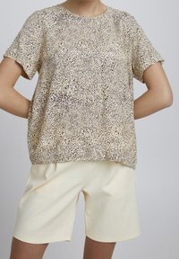 Kortärmad topp i ett beige och brunt djurmönster, tillverkad av mjukt tyg. Kombinerad med ljusbeiga shorts med elastisk midja.