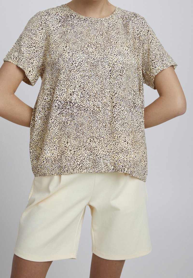 Kortärmad topp i ett beige och brunt djurmönster, tillverkad av mjukt tyg. Kombinerad med ljusbeiga shorts med elastisk midja.