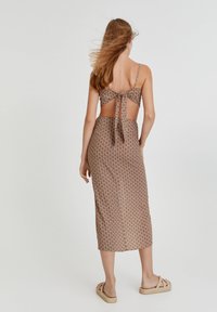 Abito midi marrone con motivo, dalla schiena legata, spalline sottili e vita aderente. Presenta una texture di tessuto liscia e un design fluido.