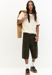 Beige t-shirt met paarse rand, donkergroene geruite shorts, bruine schoenen met dikke zool, zilveren sieraden, een tan jas over de schouder.