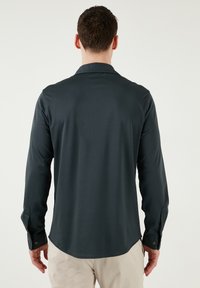 Donkergrijs langarm shirt met een zachte textuur, spitse kraag, knoopmanchetten en een afgeronde zoom. Minimalistisch ontwerp zonder zichtbare patronen.