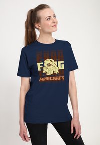 Námořnická modrá tričko vyrobené z bavlny, se grafickým designem inspirovaným Minecraftem v žluté a hnědé barvě. Krátké rukávy, volný střih.