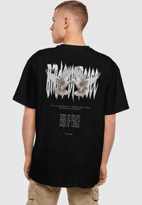 Sort kortærmet T-shirt med et grafik af to hvide duer og fed tekst. Designet inkluderer et struktureret tryk og dekorativ skrift.