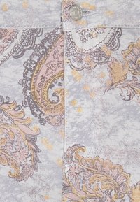 Närbild på ett mönstrat tyg med ett paisleymönster i grå, rosa och gyllene toner med inslag av gult. Strukturerat, vävt material.