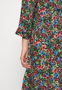 Blommig klänning med svart bakgrund och livliga röda, blå och gröna blommor. Inkluderar en knappknäppning vid ärmarna och en rynkad midjedetalj.