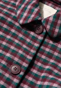 Košulja od vunenog flanela s kariranim uzorkom u tamnocrvenoj i zelenoj boji, s ovratnikom i tamnocrvenim dugmadi za zatvaranje. Mekana tekstura.
