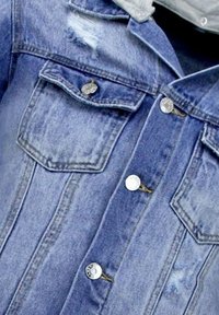 Lichtblauwe denimjas met twee borstzakken, zilveren knopen en verwerkte details. Voorzien van een klassieke kraag en textuurstof.