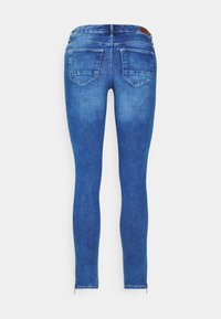 Modré džínové skinny džíny z pohledu zezadu s dvěma zadními kapsami, poutky na opasek a zipy na kotnících na bílém pozadí.