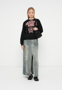 Zwarte sweatshirt met roze print, gecombineerd met een spijkerrok in slangenprint met een hoge split en versleten details. Zwarte schoenen en tas.