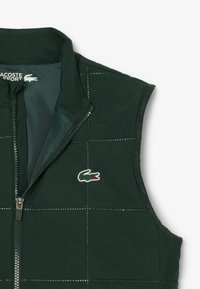 Groene gewatteerde vest met een ritssluiting aan de voorkant, gemaakt van lichtgewicht stof. Beschikt over een klein geborduurd krokodillenlogo en een staande kraag.