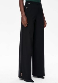 Zwarte brede broek met hoge taille, zilveren knoopaccenten aan de zijkanten en een gladde, gestructureerde stof.