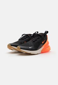 Fekete sportcipők, hálós felsőrésszel, narancssárga díszítéssel és fehér Nike logóval. Párnázott talppal rendelkezik, textúrázott tapadással és átlátszó sarkával.