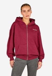 Bordo zip-up džemperis, pagamintas iš medvilnės mišinio, turintis didelį gobtuvą, priekinę kišenę ir raukšlėtus rankogalius. "PEGADOR" logotipas baltos spalvos.