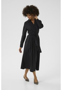 Black, long-sleeve shirt dress with a button-down front and tied waist. Features a collared neckline and a full-length, flowing skirt.