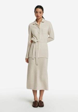 Strick-Zweiteiler in hellbeige, bestehend aus einem blusigen Oberteil mit Knopfleiste und zwei Brusttaschen sowie einem taillierten Gürtel, kombiniert mit einem passenden bodenlangen Rock.