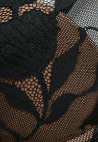 Zwart bloemenkantontwerp met ingewikkelde bladdessins, die zich over een tan mesh achtergrond met een gevarieerde structuur bevinden.