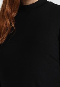 Svart överdel med hög hals skräddarsydd i ett slätt, stretchigt tyg. Har en figurnära design med en ren silhuett och minimala detaljer.