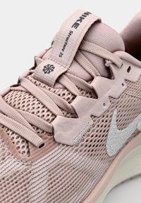 Light pink Nike sneakers featuring a mesh upper, rubber sole, textured accents, and a silver swoosh logo. Structured lacing system and branding tag.