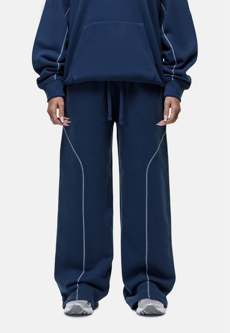 Marineblauwe oversized hoodie met een voorzak, gecombineerd met wijde sweatpants met contrasterende witte stiksels en een elastische tailleband.