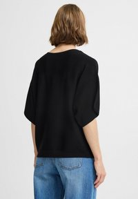Sweatshirt noir surdimensionné avec des manches courtes et larges. Texture douce, ourlet côtelé, associé à un jean droit bleu clair. Design simple et minimal.