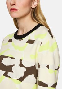 Musterpullover mit Camouflage-Design in Creme, Braun und Neon-Grün. Gerippter schwarzer Ausschnitt, weiche Textur mit lockerer Passform.