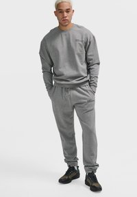 Grauer Pullover und passende Jogginghose aus Baumwollmischung. Verfügt über einen Rundhalsausschnitt und einen Kordelzugbund. Schwarzer Drucktext als Akzent.