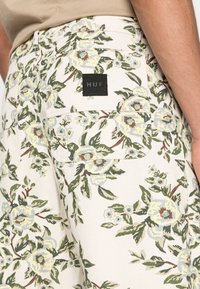 Floral-patterned shorts with a light beige background, featuring blue and green flowers, a rear pocket, and a black "HUF" label.