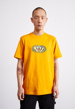 T-shirt in cotone giallo con logo grafico circolare blu e bianco al centro. Maniche corte e scollatura rotonda.